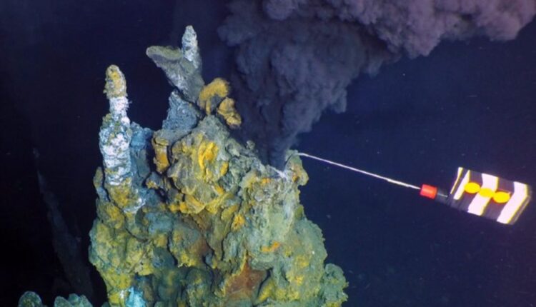 black, mineral-filled water shown spewing out of a hydrothermal vent that a robot is collecting samples from