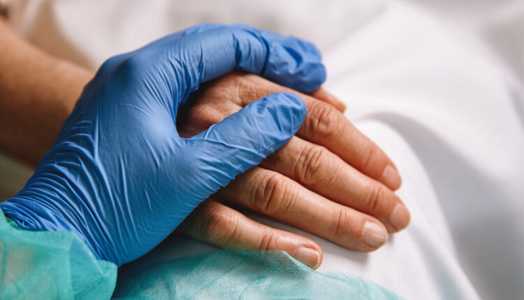 Close up of a doctor hand with blue glove giving support and love to a patient at hospital. Coronavirus pandemic concept.